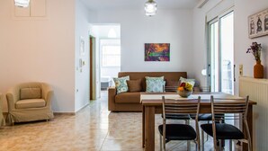 A living room with a sofa, a dining table with chairs, and a window with a view. - Kantouni 2 Heraklion Apartment (Heraklion)