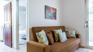 A brown sofa with floral cushions in a room with a white wall and a painting above it. - Kantouni 2 Heraklion Apartment (Heraklion)
