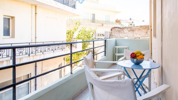 A balcony with a table and chairs, a bowl of fruit, and a view of buildings. - Kantouni 2 Heraklion Apartment (Heraklion)