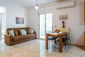A living room with a sofa, a dining table with chairs, a pendant light, and a radiator. - Kantouni 2 Heraklion Apartment (Heraklion)