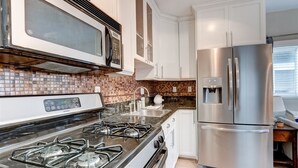 A modern kitchen with a stainless steel refrigerator, a microwave, and a gas stove. - Waypoint Cottage, one block from the beach! (San Diego)
