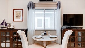 A dining area with a round table, two chairs, a television, and a cabinet with glass doors. - Waypoint Cottage, one block from the beach! (San Diego)