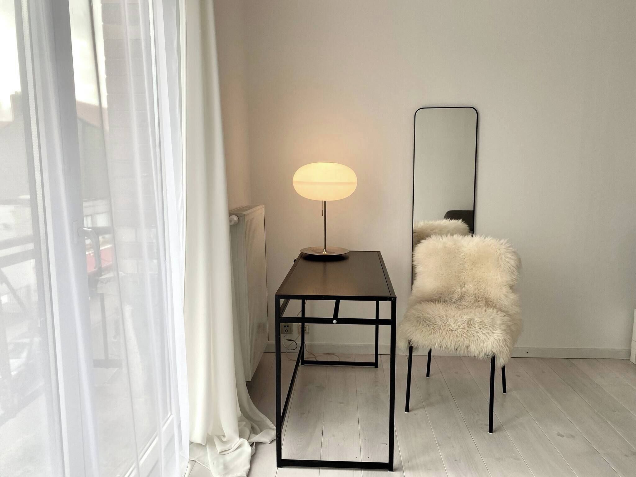 Une pièce avec un lampadaire, un fauteuil moelleux, un miroir et un radiateur.