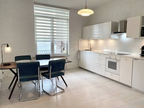A modern kitchen with white cabinets, a dining area with a table and chairs, and a large window with blinds. - Wit II, Near Metro, Train N7670 (Brussels)
