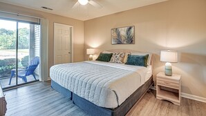 A bedroom with a large bed, two bedside lamps, a ceiling fan, and a view through a sliding glass door to the outside. - Pawleys Island Condo w/ Screened Porch + Golfing! (Pawleys Island)