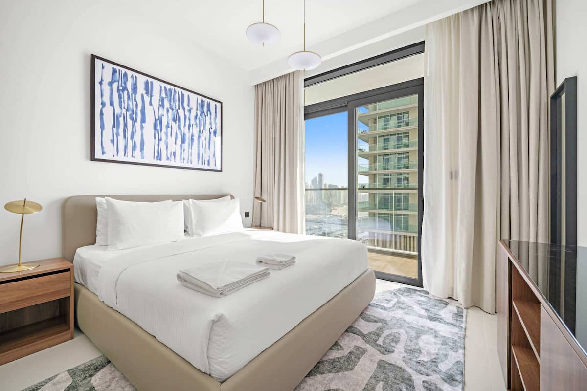 Un hotel moderno con una cama grande, un televisor de pantalla plana, un cuadro en la pared y vistas a la ciudad desde la ventana.