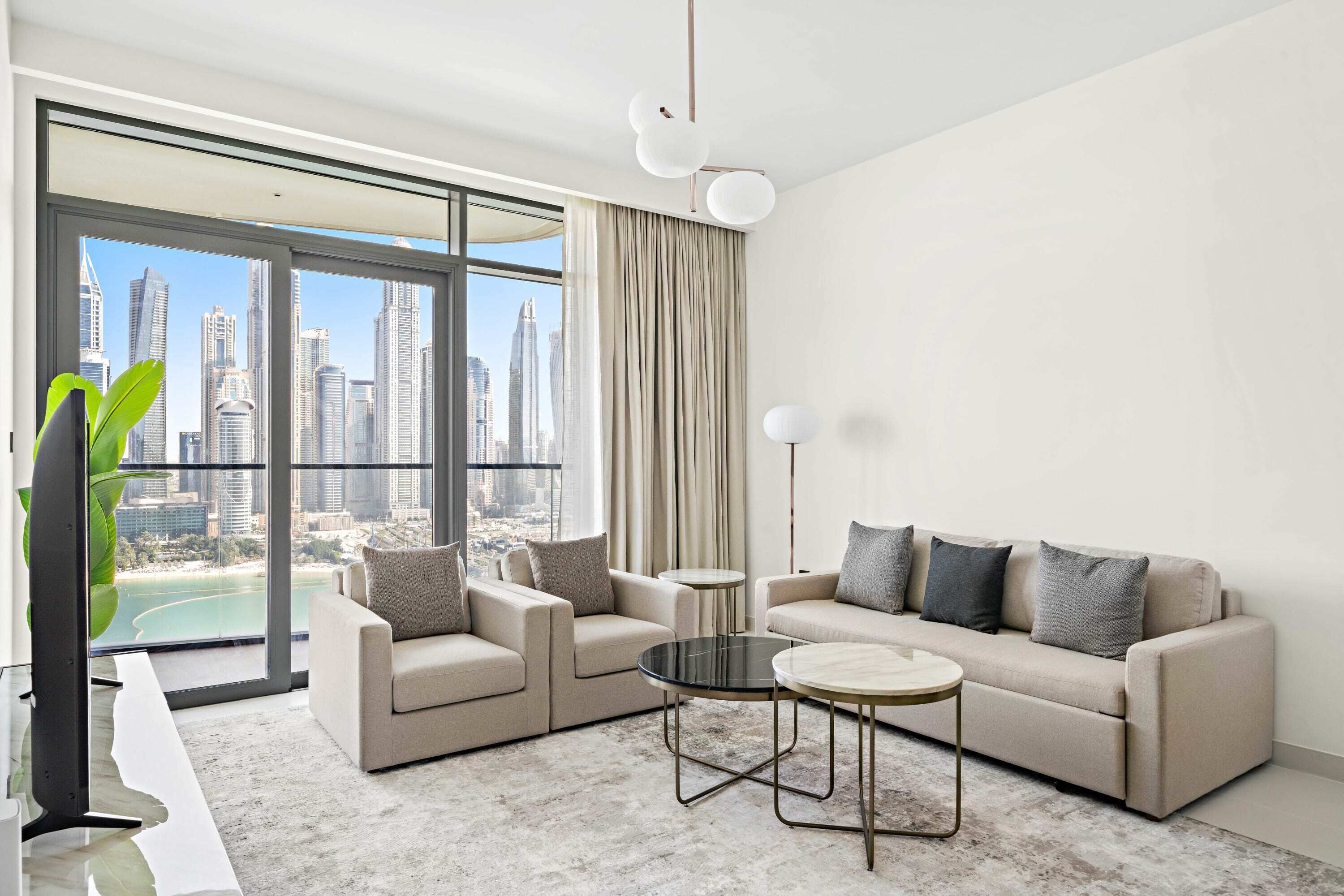 A modern living room with a sofa, two armchairs, and a coffee table. Large windows offer a view of a cityscape and a body of water.
