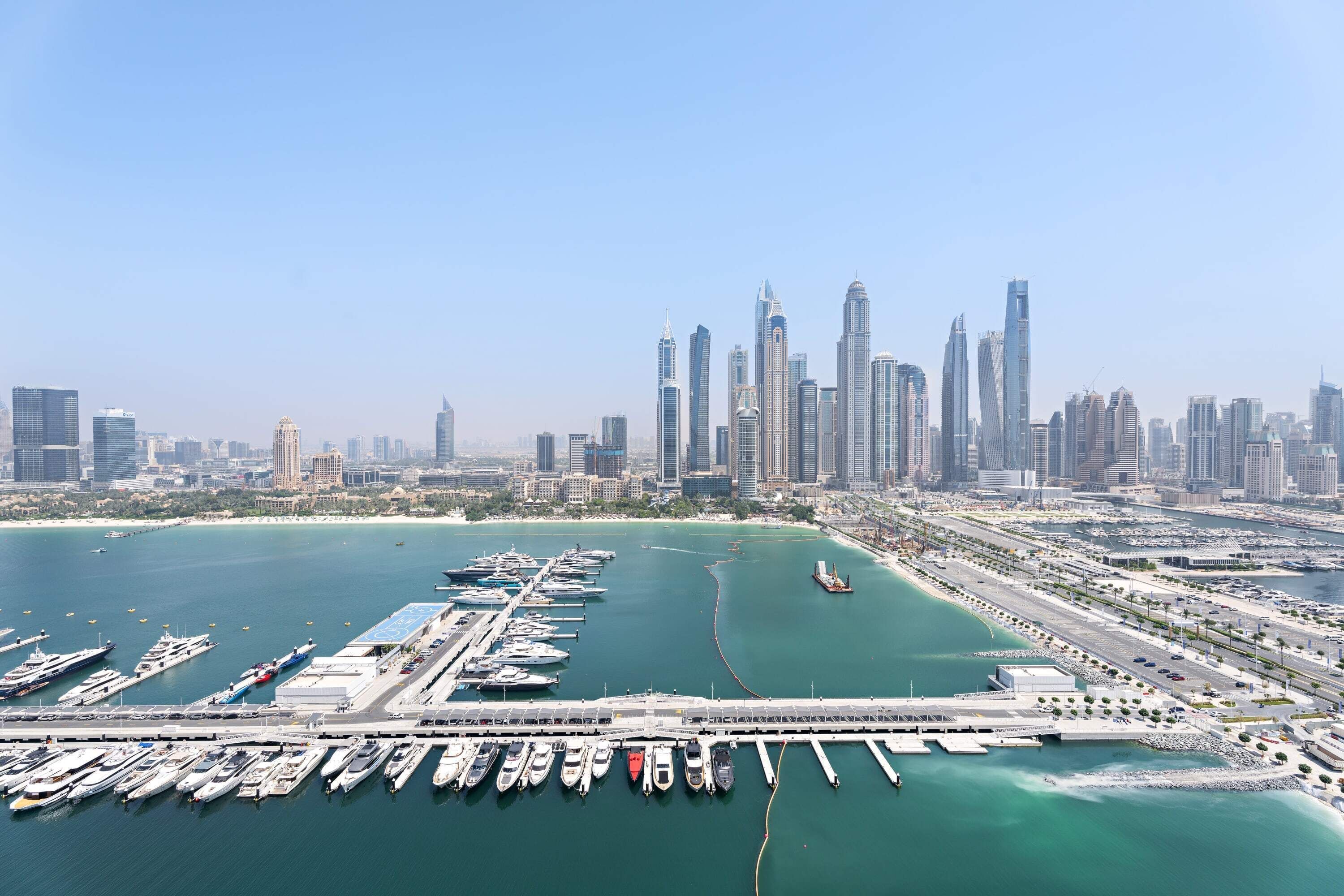 A marina with numerous boats docked, a bridge connecting to the city, and a skyline of modern skyscrapers.