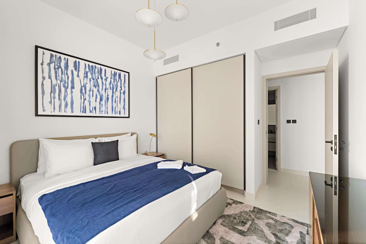 Una habitación de hotel moderna con una cama grande, una mesita de noche, un armario y un escritorio con cubierta de vidrio.