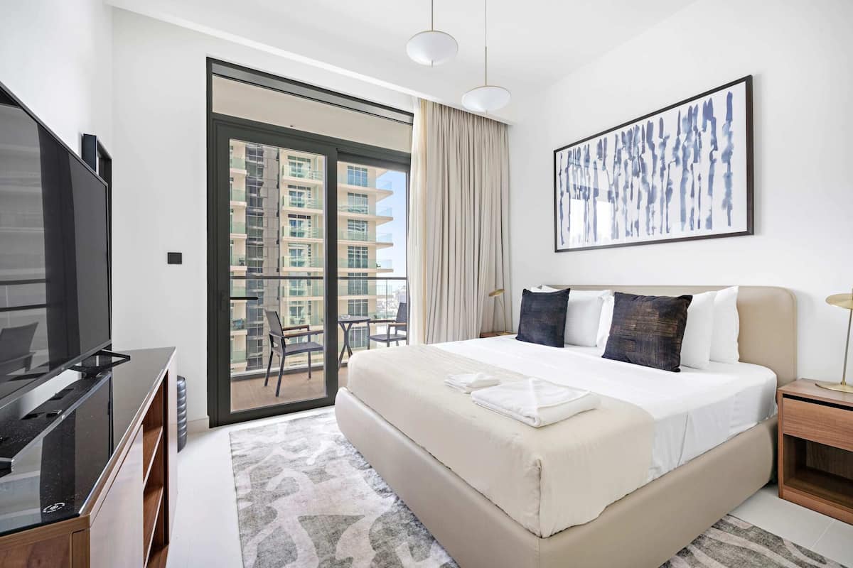 Habitación de hotel moderna con una cama grande, un televisor de pantalla plana, un balcón con vistas a la ciudad y un cuadro abstracto enmarcado.