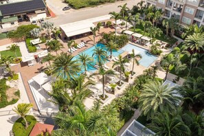 Un hôtel doté d’une piscine entourée de palmiers, de chaises longues et d’un espace de stationnement.
