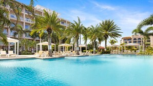 Ein Poolbereich eines Resorts mit Palmen, Liegestühlen und einem großen Gebäude im Hintergrund.