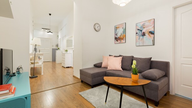 Ein modernes Wohnzimmer mit einem grauen Ecksofa, einem Holztisch und einem Fernseher auf einem türkisfarbenen Schrank.