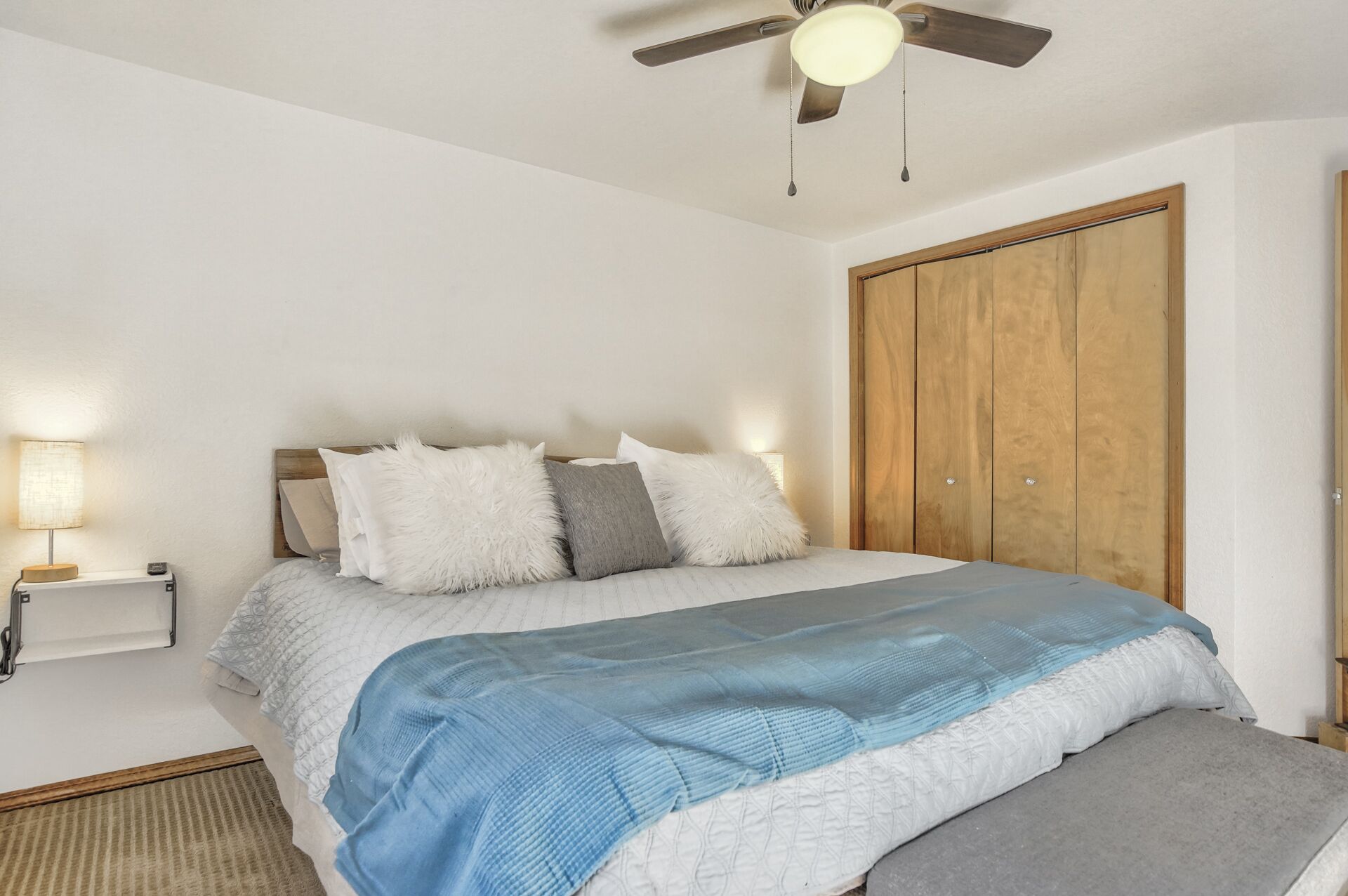 Une chambre à coucher avec un lit, un ventilateur de plafond, une armoire en bois et une lampe de chevet.