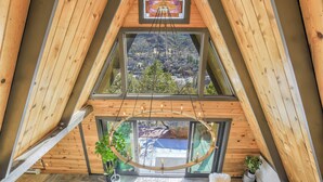 Una habitación de madera triangular con dos ventanas amplias que ofrecen vistas a un pueblo y montañas.