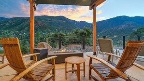 Un espacio de estar al aire libre con techo, sillas de madera y un hogar, con vistas a un paisaje montañoso.