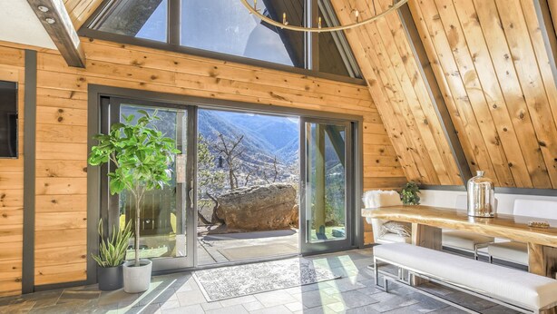 Un interior moderno con paredes de madera, puertas de cristal grandes que dan a vistas de la montaña, un banco y plantas en macetas.