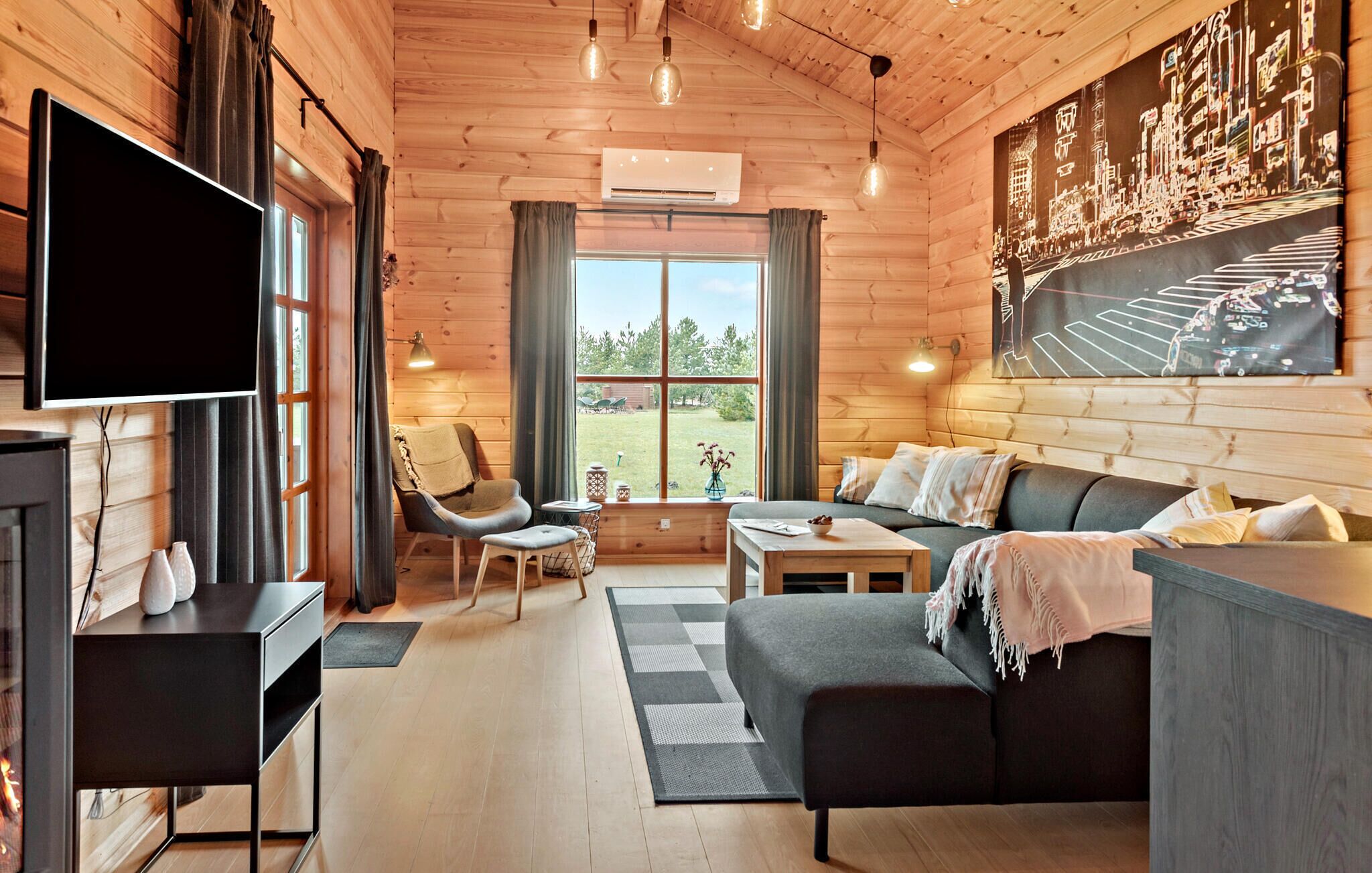 Un interior de cabaña acogedor con un ventanal grande, un sofá, una silla, un televisor y una chimenea.