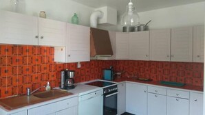 A compact kitchen with white cabinets, a red patterned backsplash, a stove, a sink, and a coffee maker. - La Villa Champenoise (Pierry)