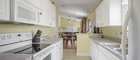 A kitchen with white cabinets, a stove, and a dining area in the background.