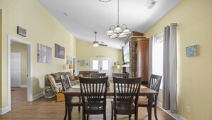 A dining area with a wooden table and chairs, a ceiling fan, and a view of the living room. - 0.3 mi. to beach, 4 BR, 3 Bath, sleeps 9, grill, pool table, games, LSV for rent (North Myrtle Beach)