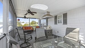 A covered outdoor dining area with a glass table, metal chairs, and a ceiling fan. - 0.3 mi. to beach, 4 BR, 3 Bath, sleeps 9, grill, pool table, games, LSV for rent (North Myrtle Beach)