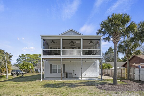 A two-story house with a balcony, a palm tree, and a car parked in the driveway.