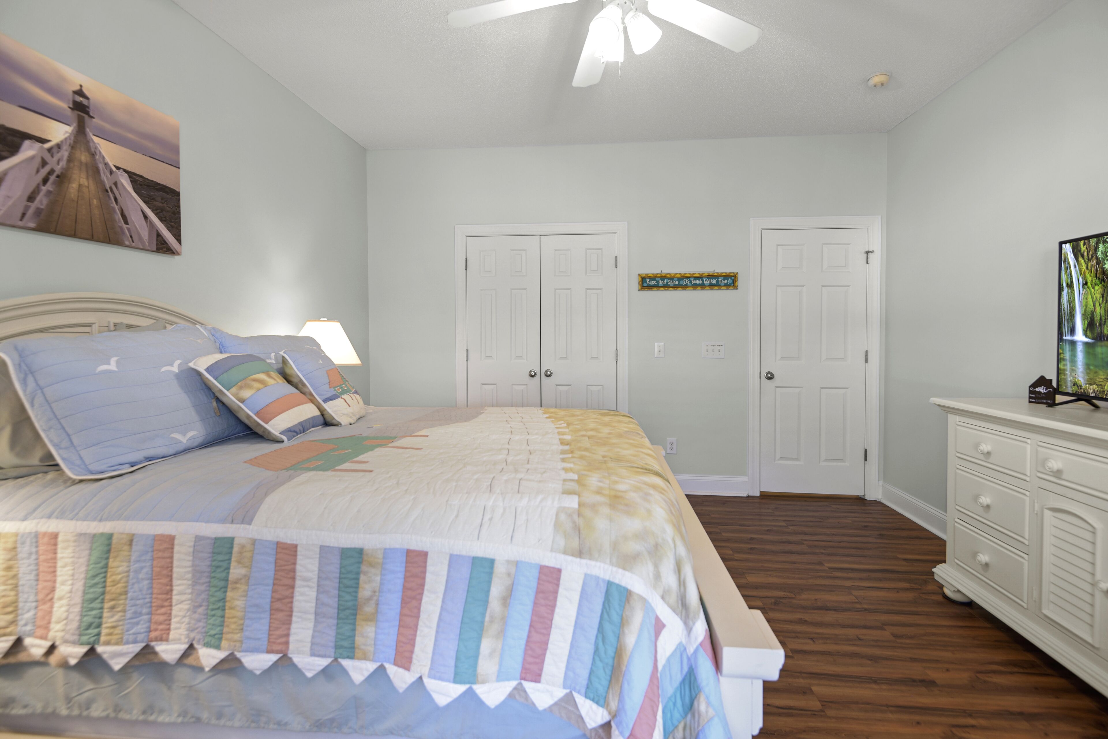 A bedroom with a bed, two doors, a dresser, and a ceiling fan.