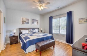Une chambre à coucher comprenant un lit, une table de chevet, un banc, un bureau, un ventilateur de plafond et une fenêtre avec des rideaux.