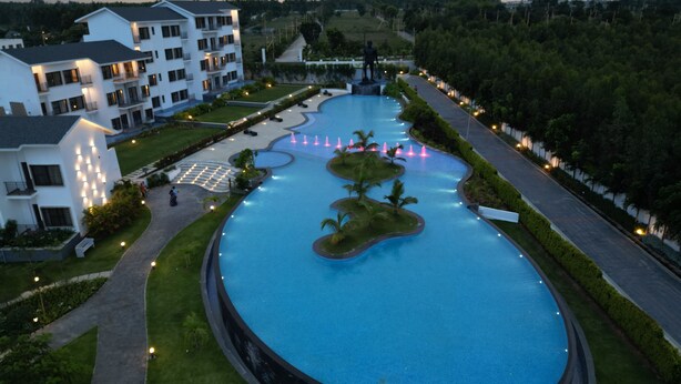 A large, oval-shaped swimming pool with a fountain, surrounded by well-maintained lawns and pathways.