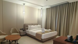 A hotel room with a bed, two chairs, a small table, a lamp, and a nightstand with a phone.