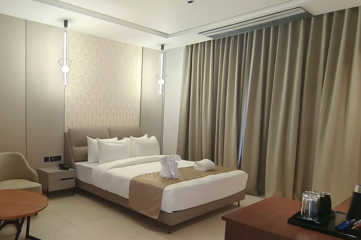 Une chambre d’hôtel avec un lit, deux chaises, une petite table, une lampe et une table de chevet avec un téléphone.
