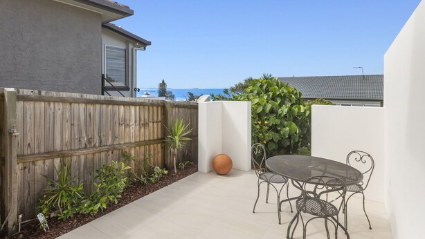 A patio with a table and chairs, a wooden fence, and a view of the ocean. - Sutherland Sunrise - Kingscliff Studio (Tweed)