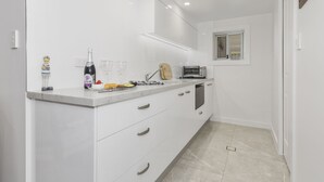 A modern kitchen with white cabinets, a marble countertop, a toaster, and a small window above the sink. - Sutherland Sunrise - Kingscliff Studio (Tweed)
