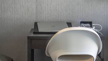 Uma mesa com um laptop, um smartphone carregando e uma cadeira branca.
