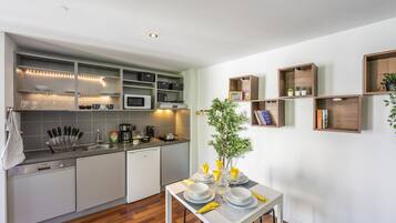 Een moderne keuken met inbouwapparatuur, een eethoek met een tafel voor vier personen, en houten planken met boeken en planten.