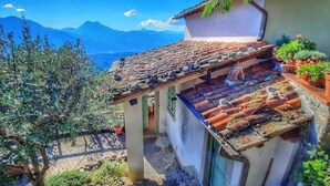 A traditional building with terracotta roof tiles, a stone staircase, and a view of mountains.