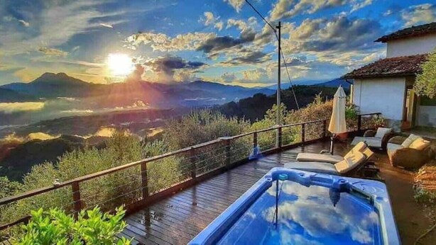 A hot tub on a wooden deck with a view of mountains and a sunset.