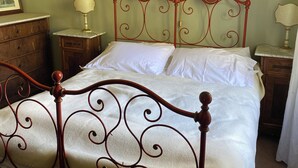 A bed with a metal frame and white bedding in a room with green walls and wooden furniture.