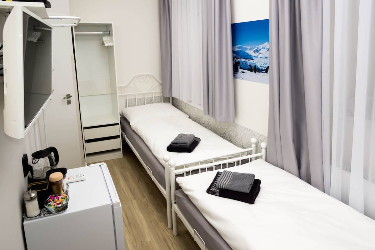 A hotel room with two single beds, a desk with a computer and a coffee maker, a wardrobe, and a window with a mountain view.