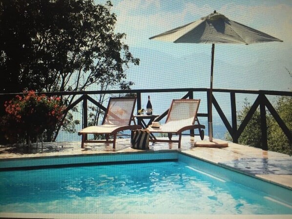 A poolside area with two lounge chairs and a table, surrounded by a railing and trees.