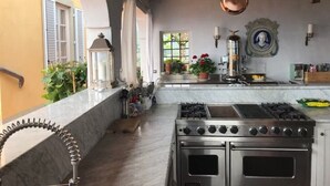 A kitchen with a gas stove, oven, marble countertop, potted plants, and a hanging copper pot.