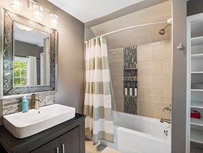 A modern bathroom with a large mirror, a white sink, a shower with a beige curtain, and a wooden vanity.