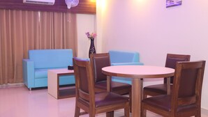 A room with a blue sofa, a wooden dining table with four chairs, a vase with flowers, and an air conditioning unit. - Janaki Star Hotel (Janakpur)