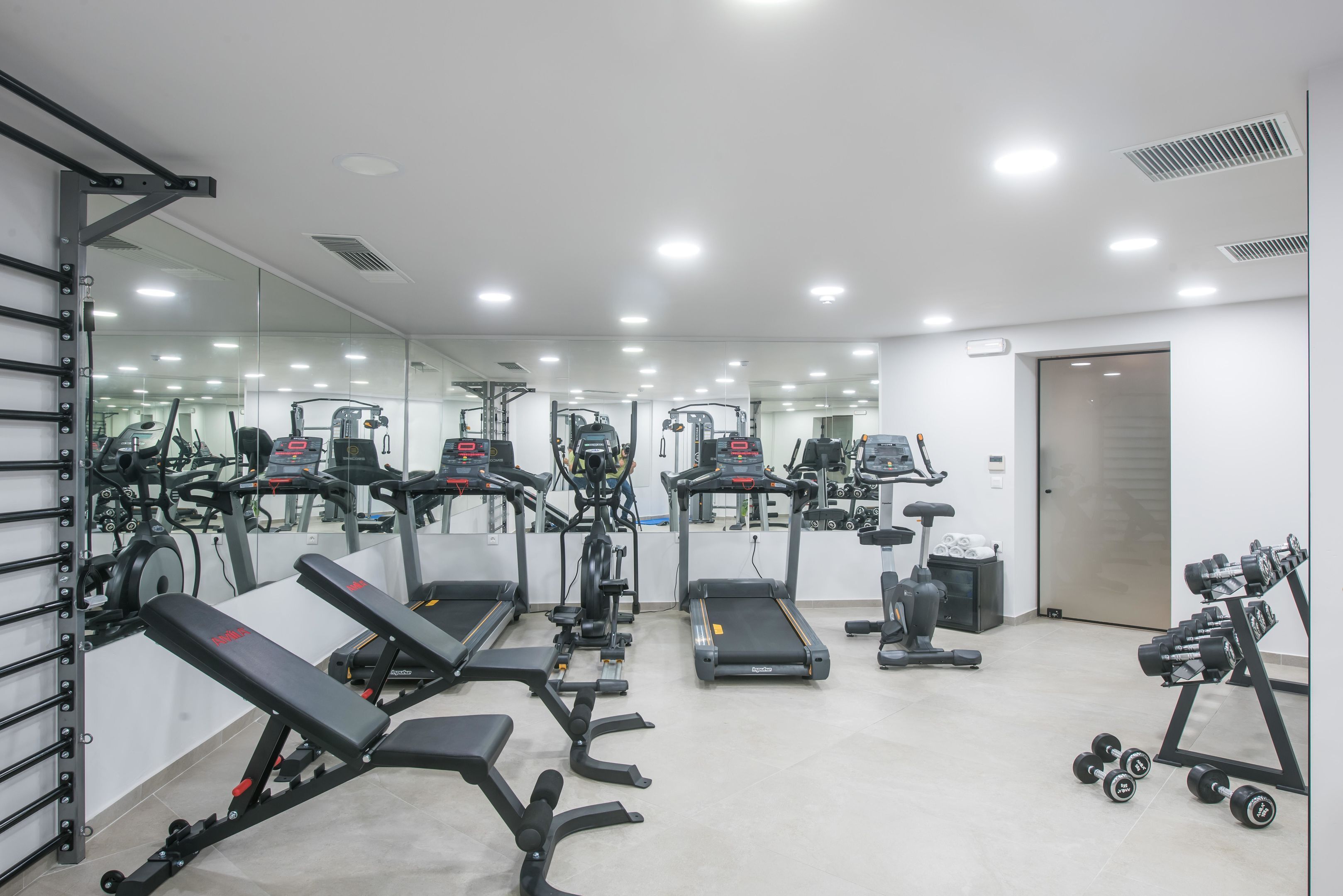 Un gimnasio con cintas de correr, una banca, mancuernas y máquinas de pesas.