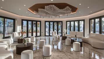 A spacious lobby with a polished marble floor, white sofas, and round ottomans arranged around a central coffee table.