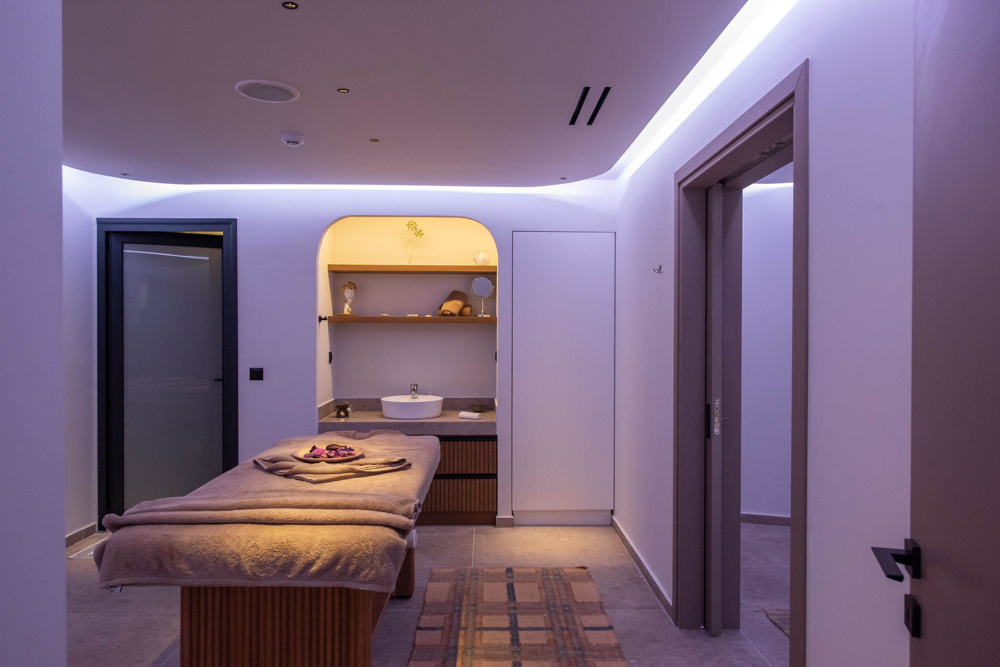 Ein moderner Spa-Raum mit Massagetisch, Waschbecken und Schminktisch.