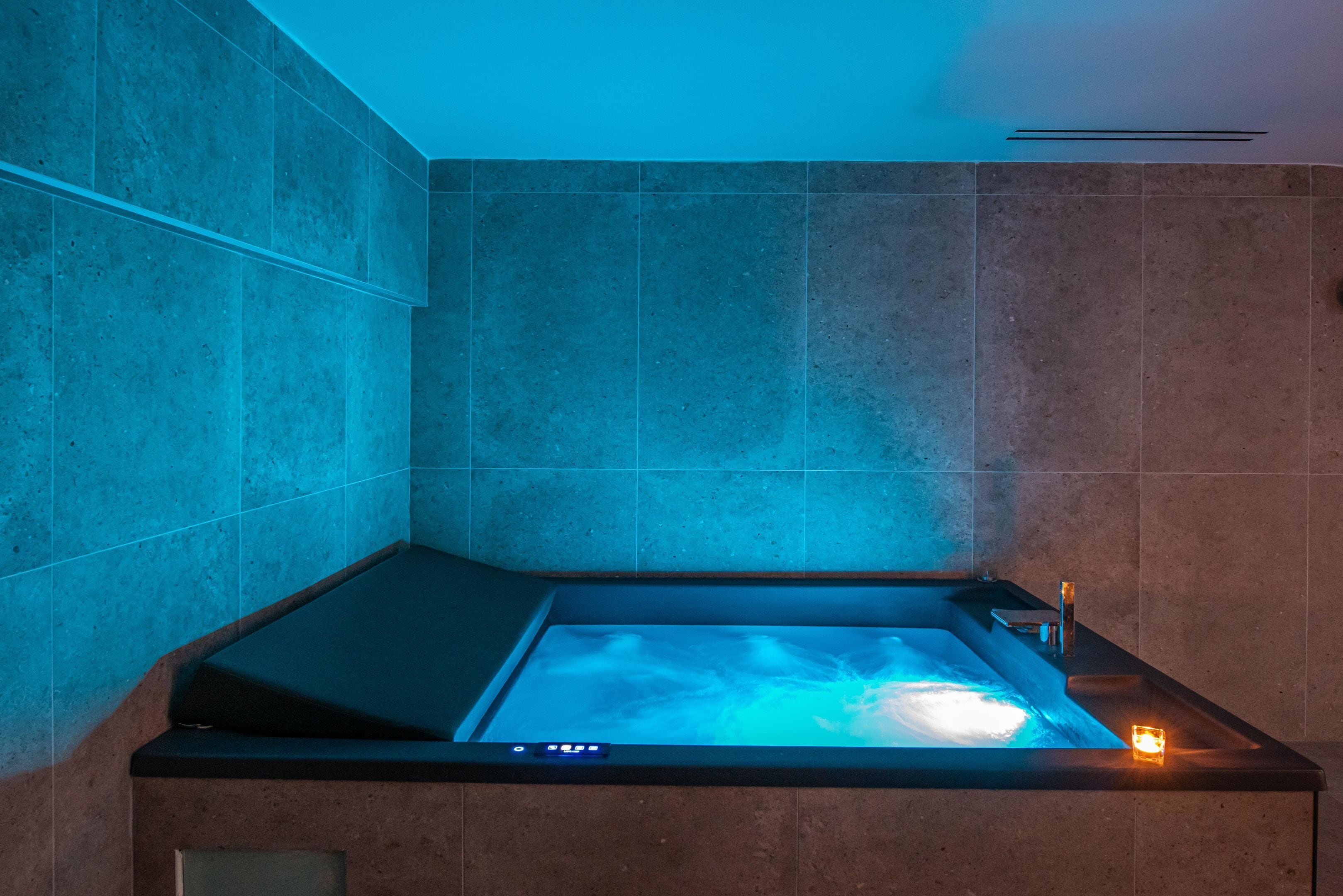 A modern bathroom with a built-in bathtub, a control panel, and a small side table.