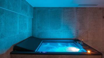 A modern bathroom with a built-in bathtub, a control panel, and a small side table.