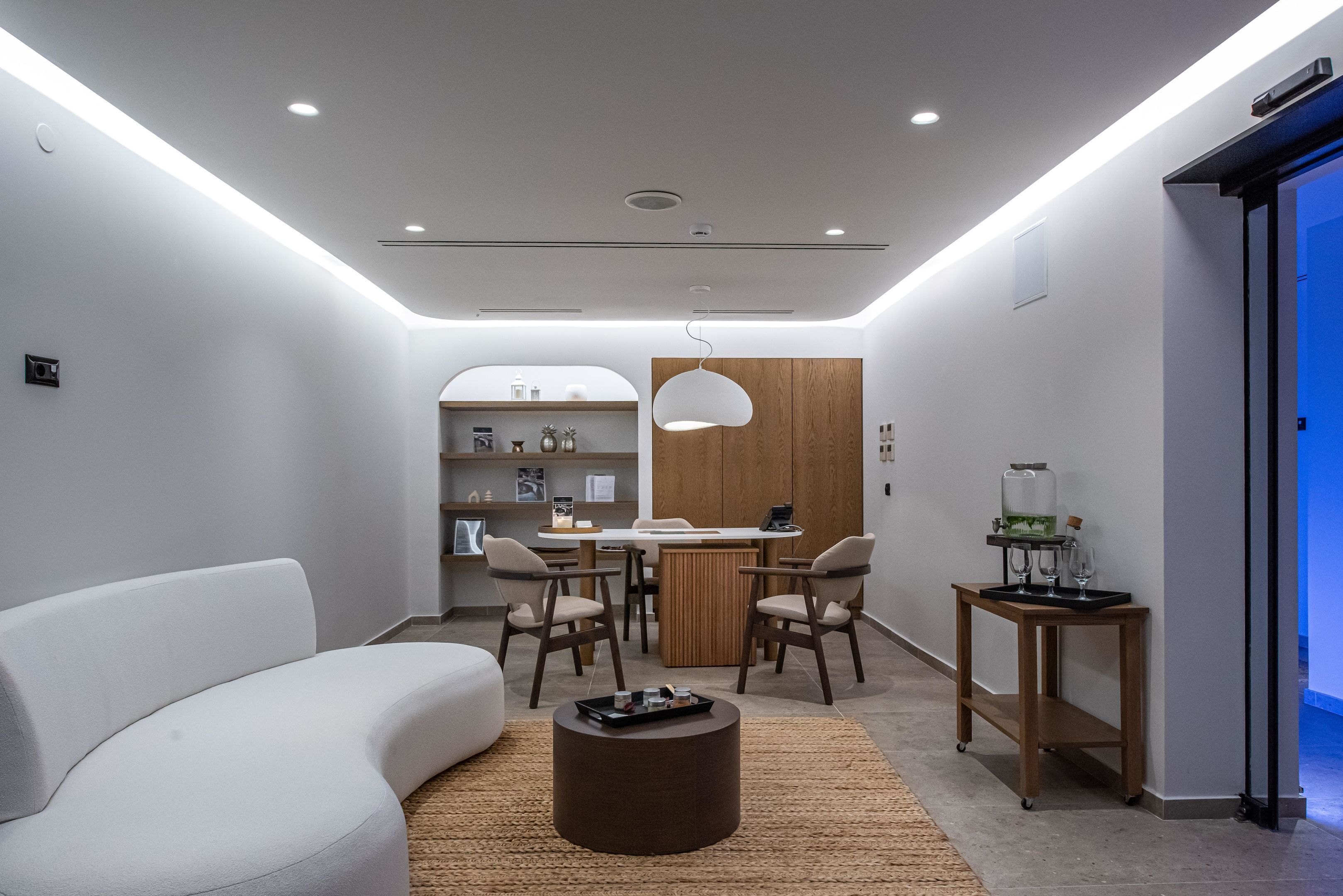 Una sala moderna con un sofá blanco, una mesa redonda de centro y un comedor con una mesa y sillas de madera.